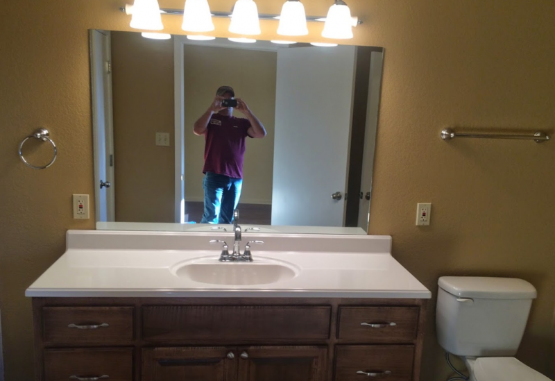 Bathroom vanity with sink, large mirror, lights, and a person taking a mirror selfie