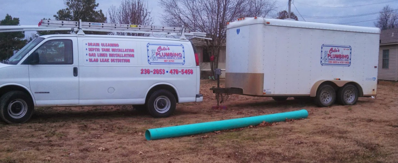 White utility van and enclosed trailer parked on dirt beside a long blue pipe in a yard