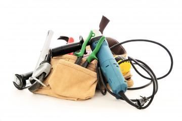 A tan tool bag filled with assorted power tools and cords on a white background