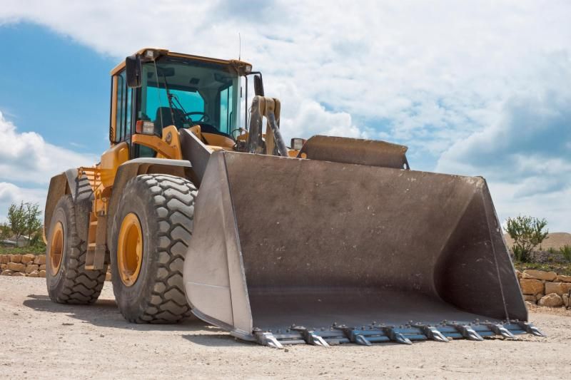 Yellow construction loader with a large bucket on a dirt site under a blue sky