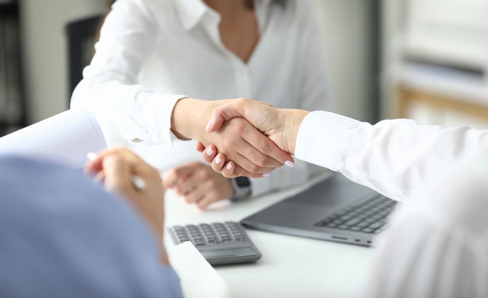 two people shaking hands in front of a laptop and calculator