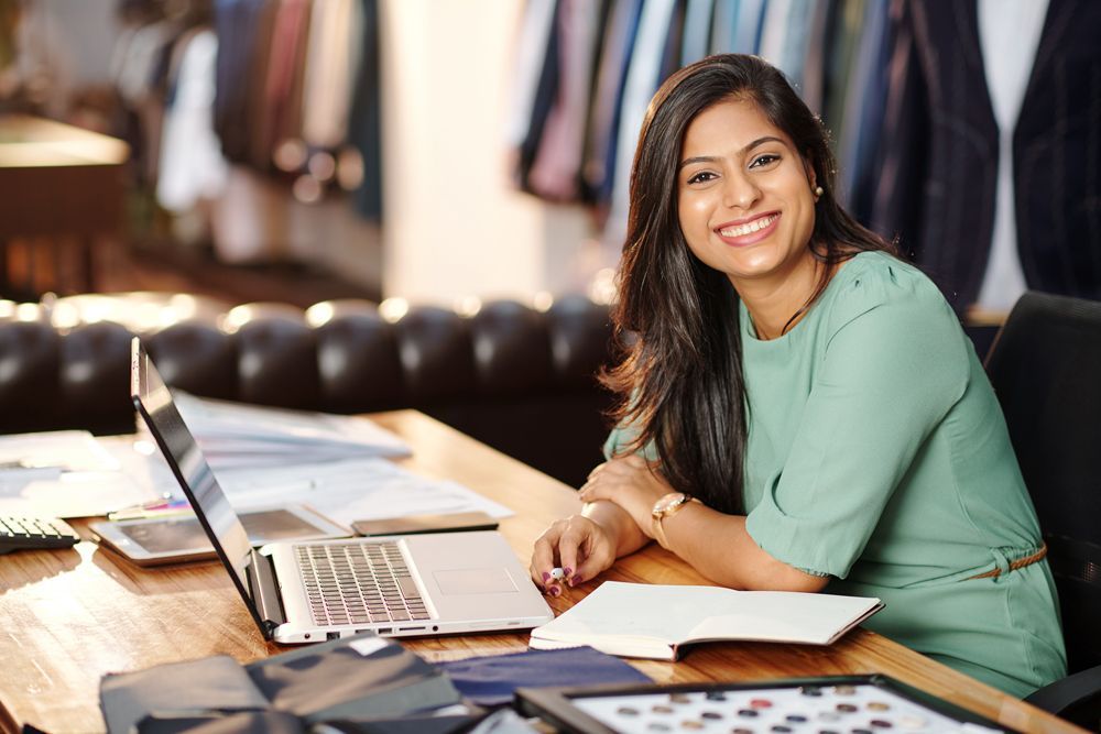a woman sits at a desk with a laptop and a notebook