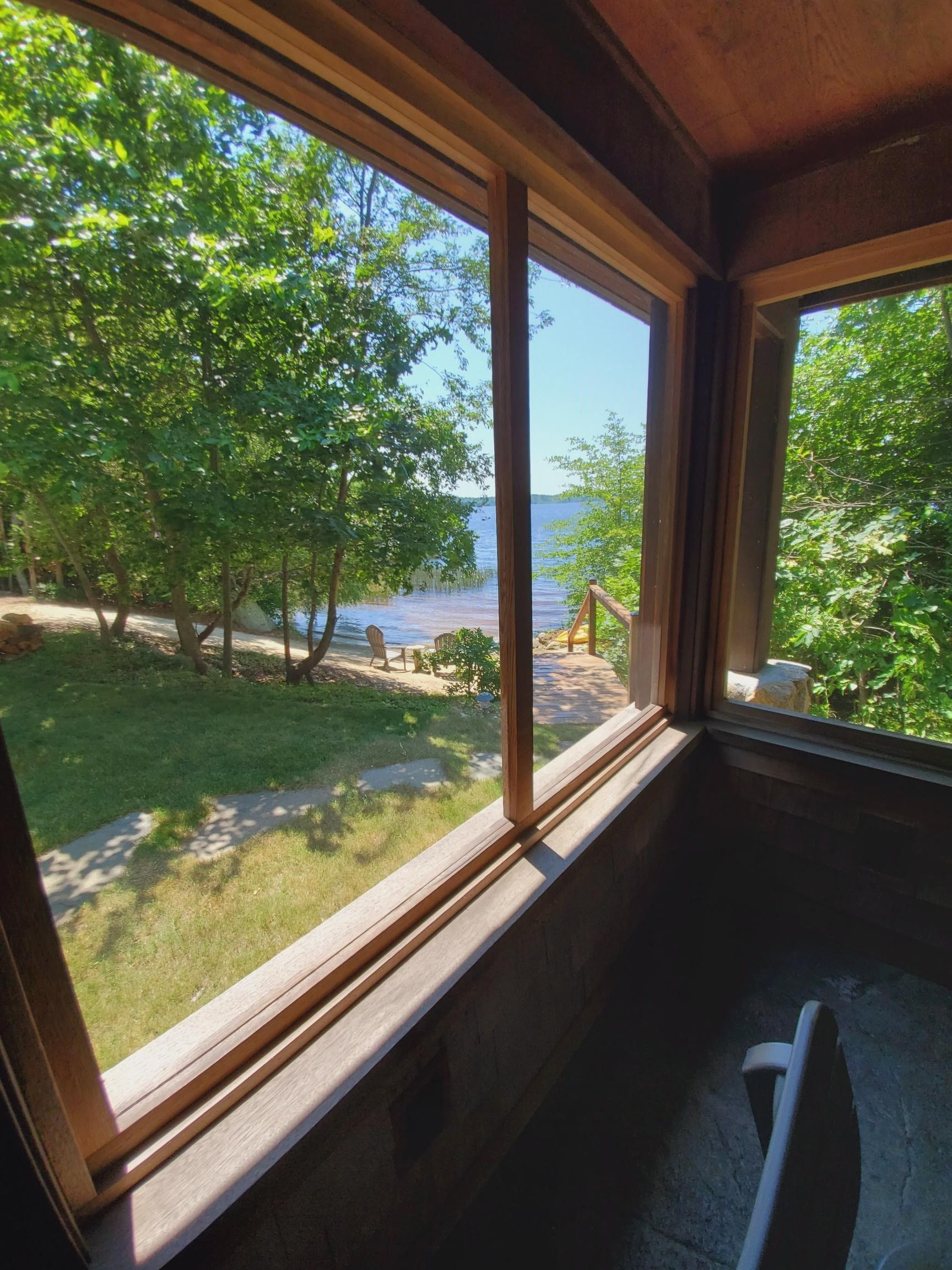 View from a wooden framed window of a lake surrounded by green trees.