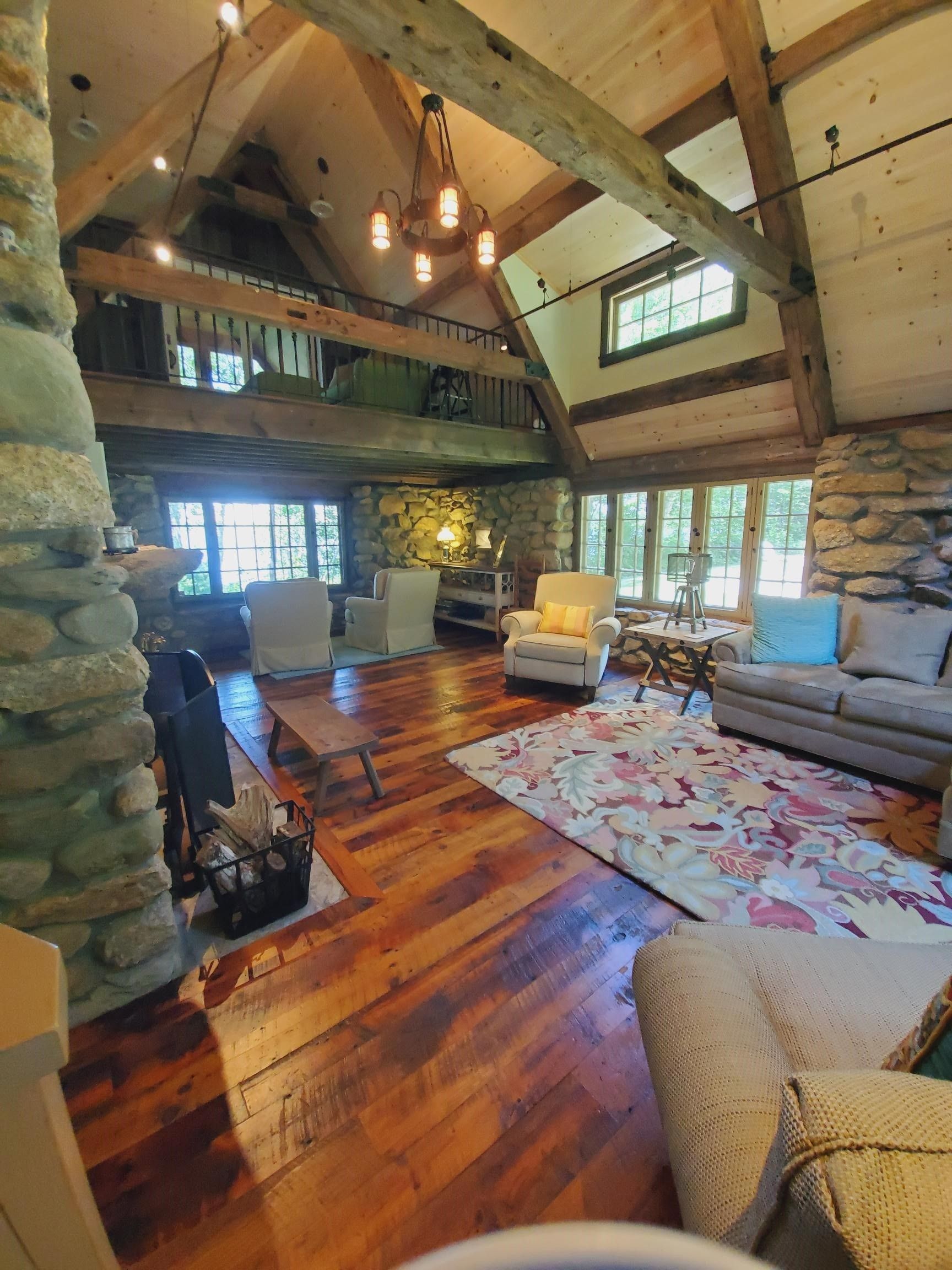 Cozy cabin living room with stone walls, wooden beams, hardwood floors, and a colorful rug.