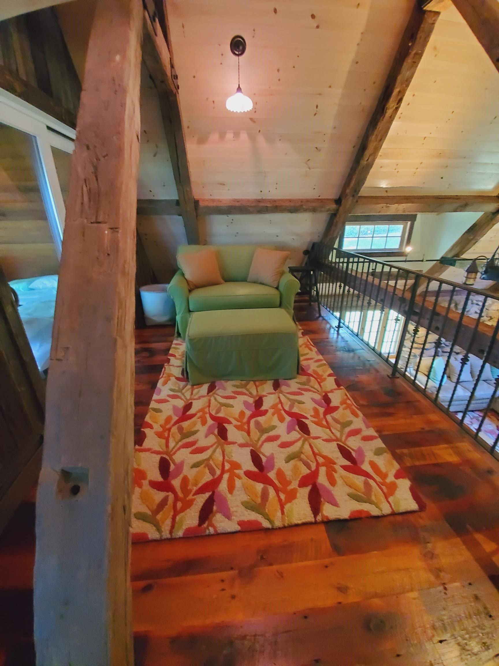 Cozy loft seating area with a green chair and ottoman on a patterned rug; exposed wooden beams.
