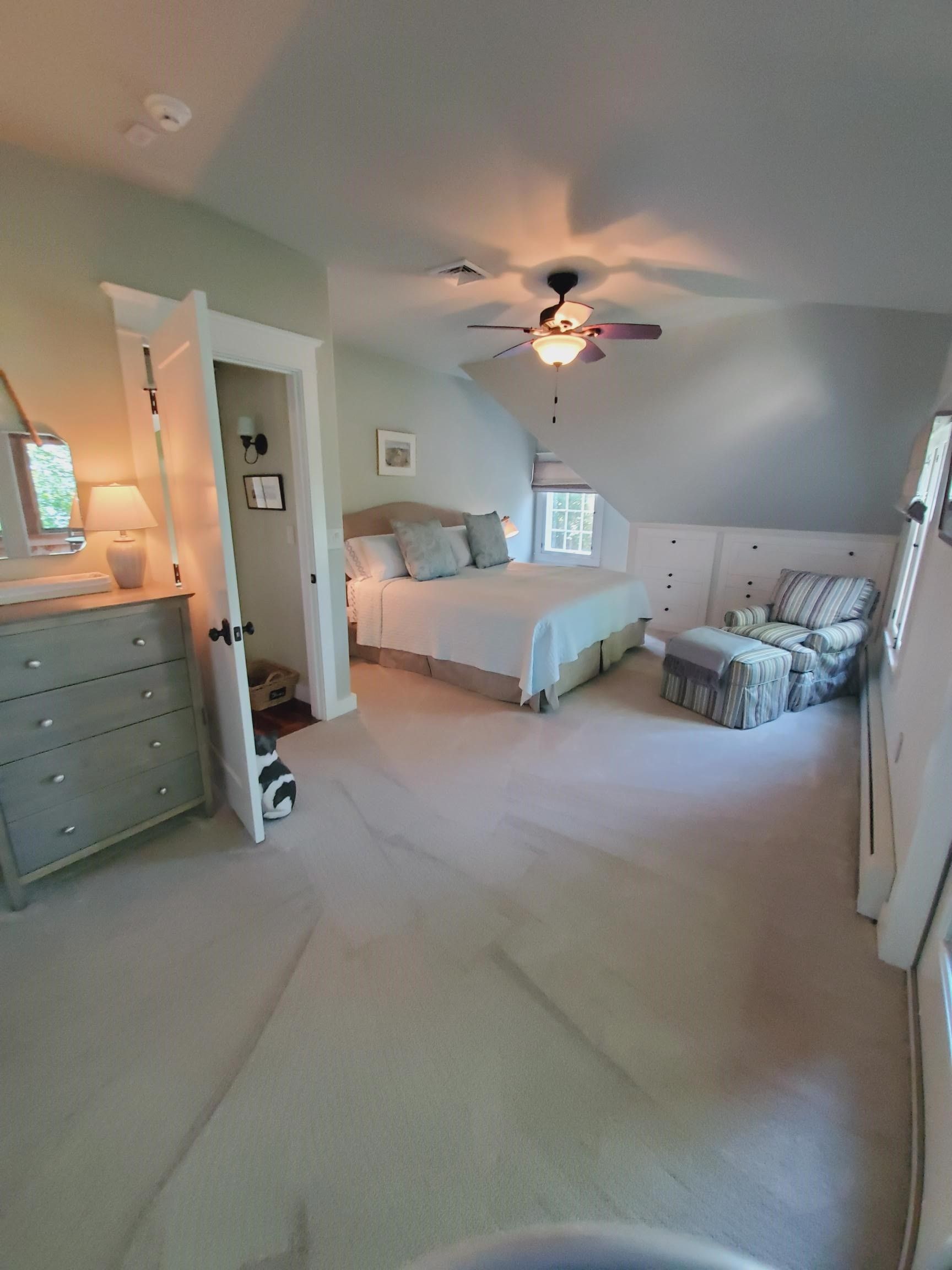 Bedroom with light gray walls, a bed, dresser, chair, and overhead fan.