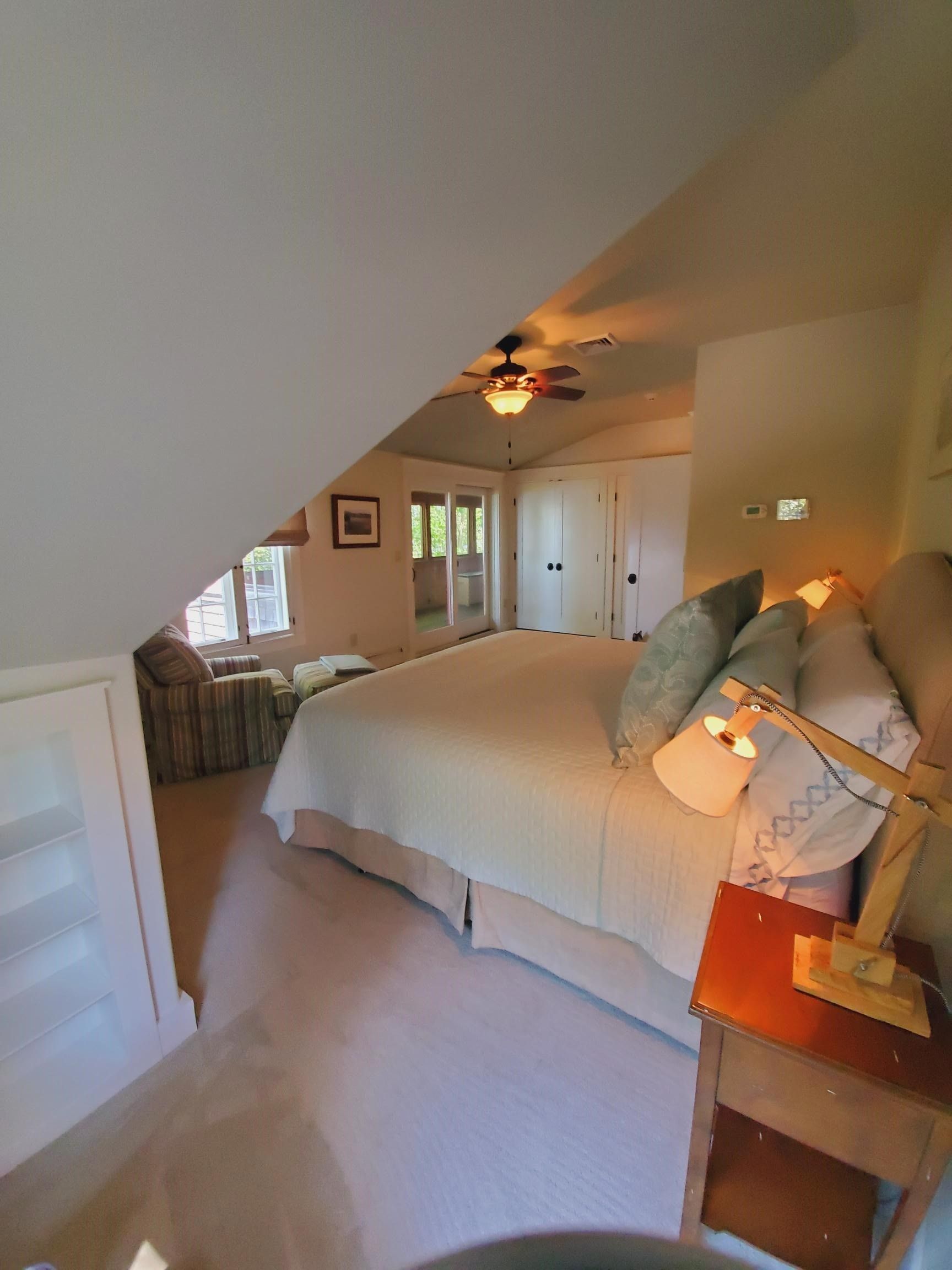 Bedroom with white bed, beige walls, and window seat under a sloped ceiling.