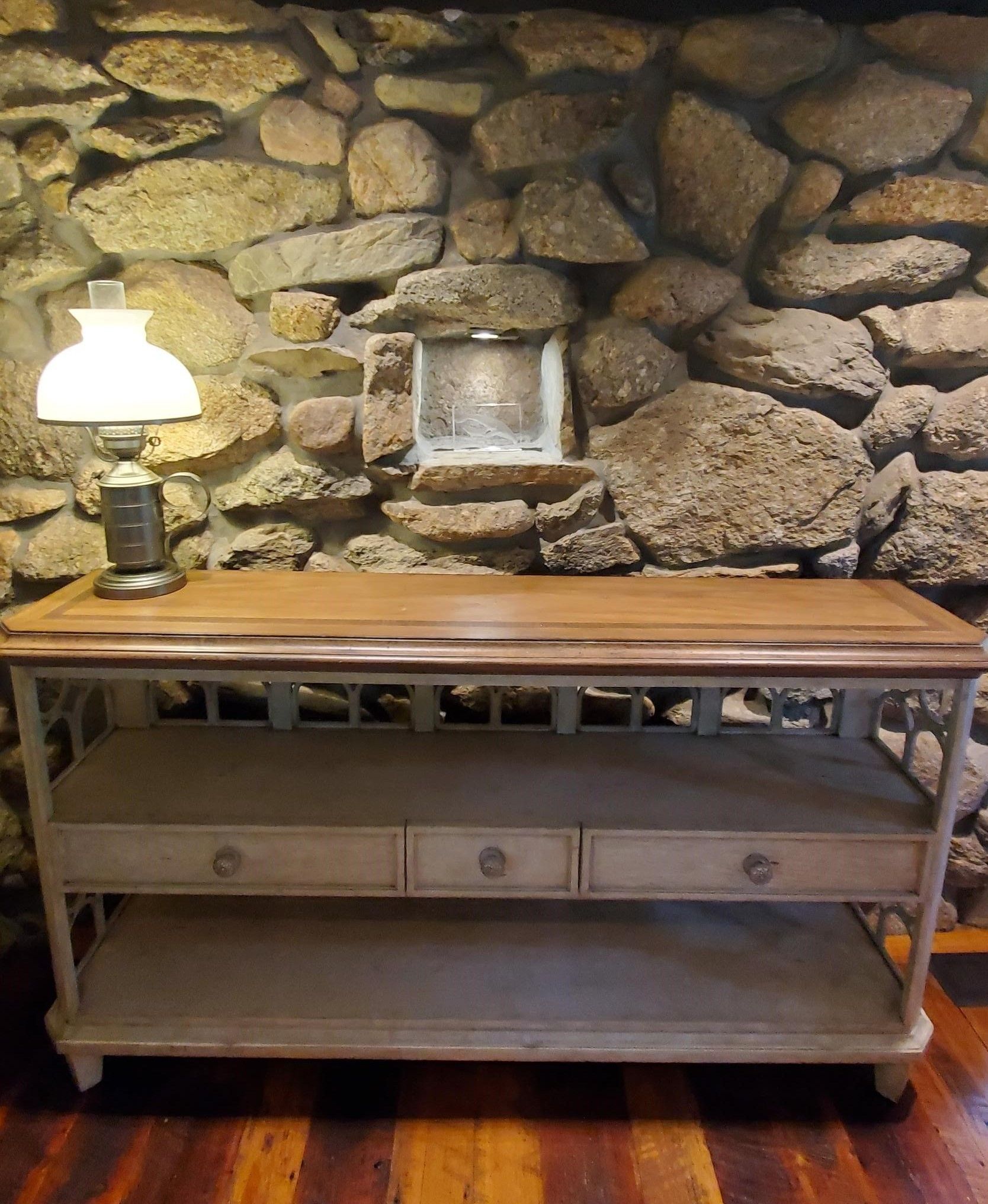 Wooden console table with drawers and lamp in front of a stone wall.