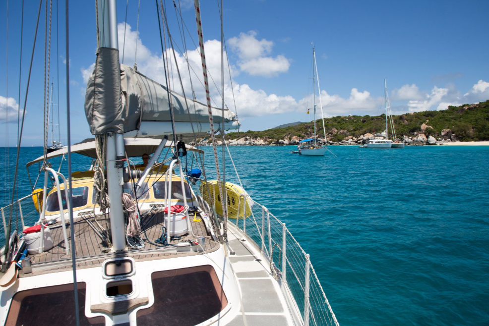 Sailboat anchored off a Caribbean island with turquoise water, rocky shoreline, and sandy beach.
