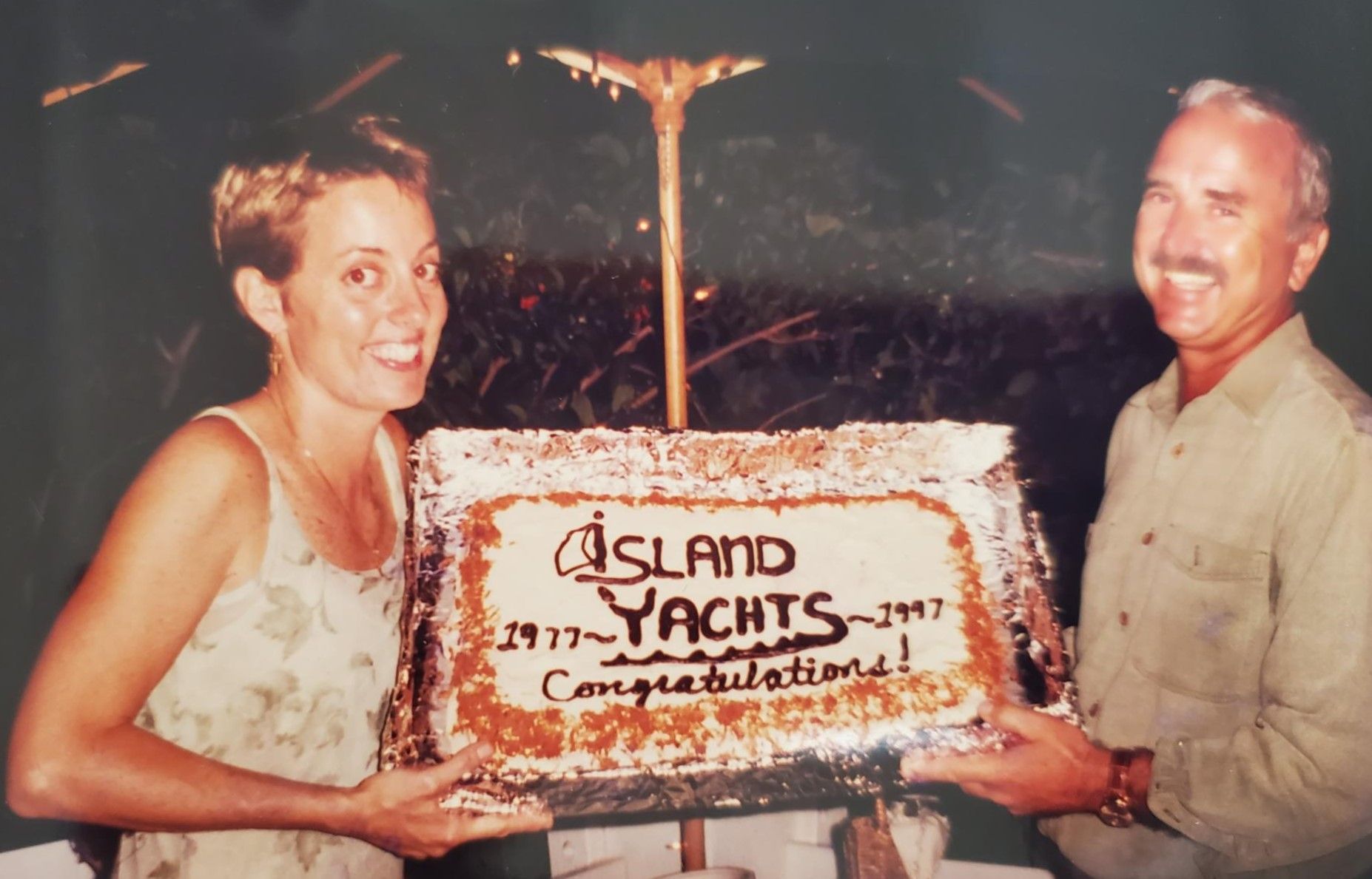 A man and a woman holding a cake that says island yachts