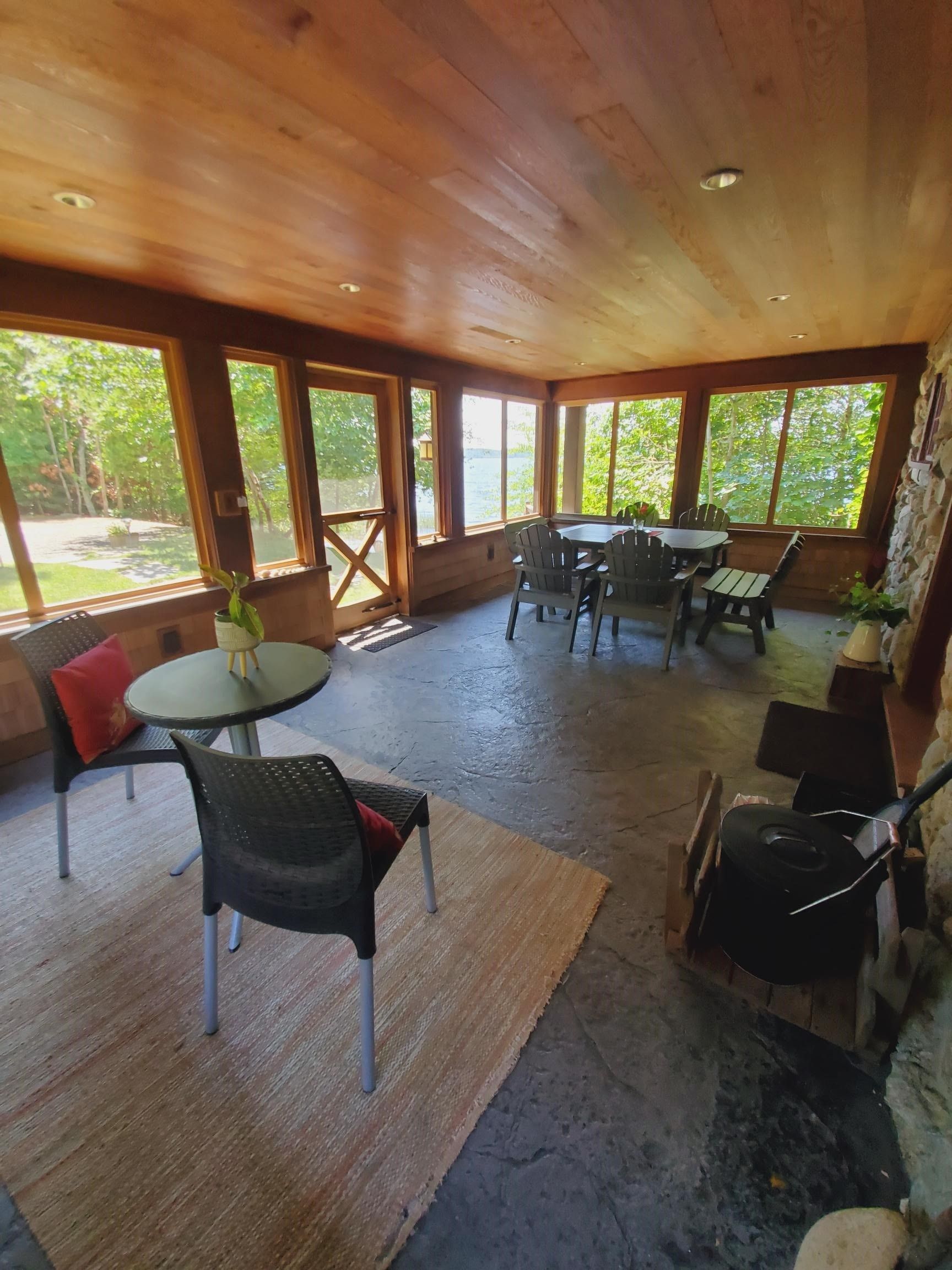 Screened porch with wooden ceiling and trim, stone accent wall, and multiple seating areas with views of the outdoors.