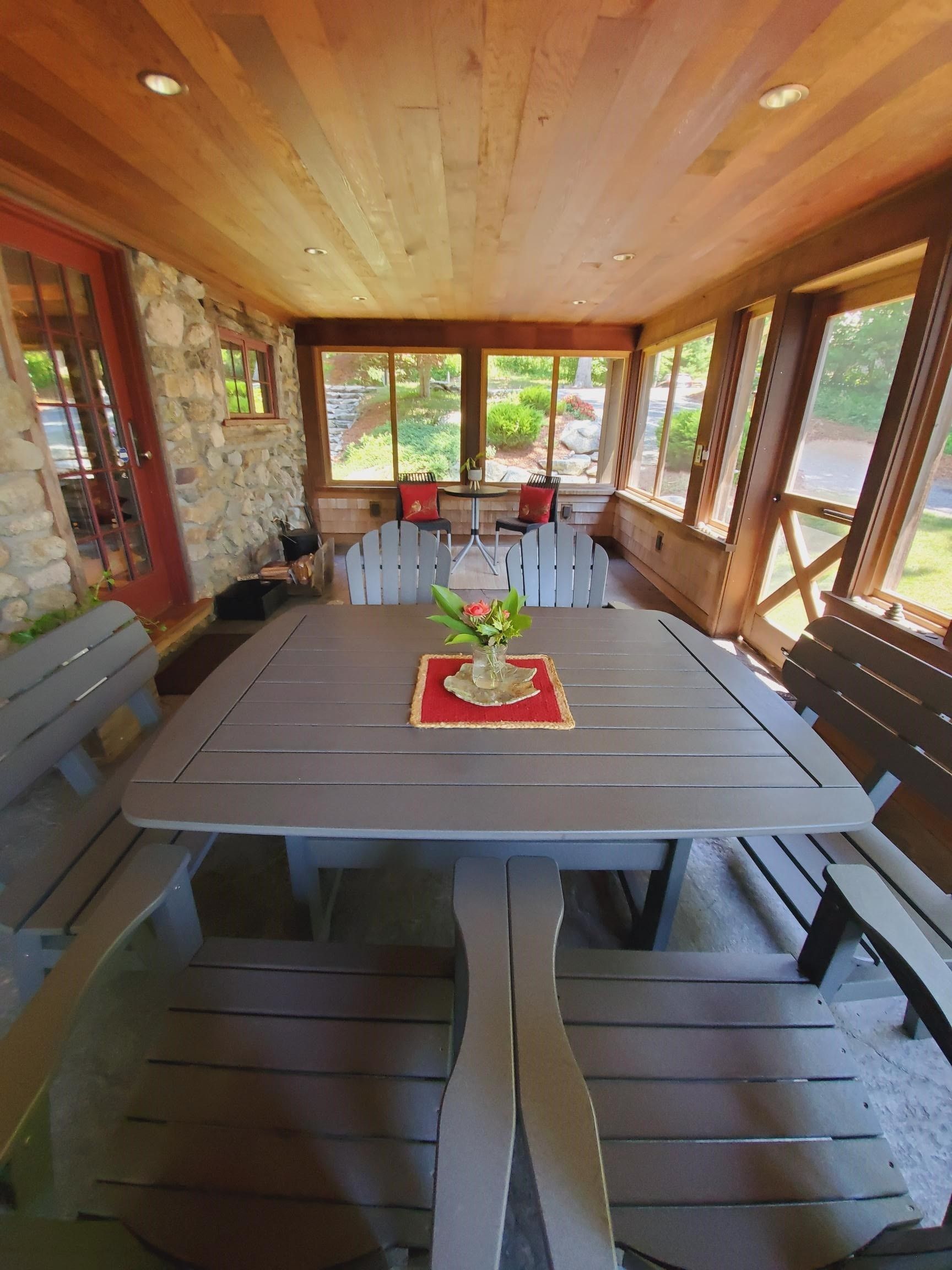 Screened porch with large gray picnic table, benches, stone wall, and windows.