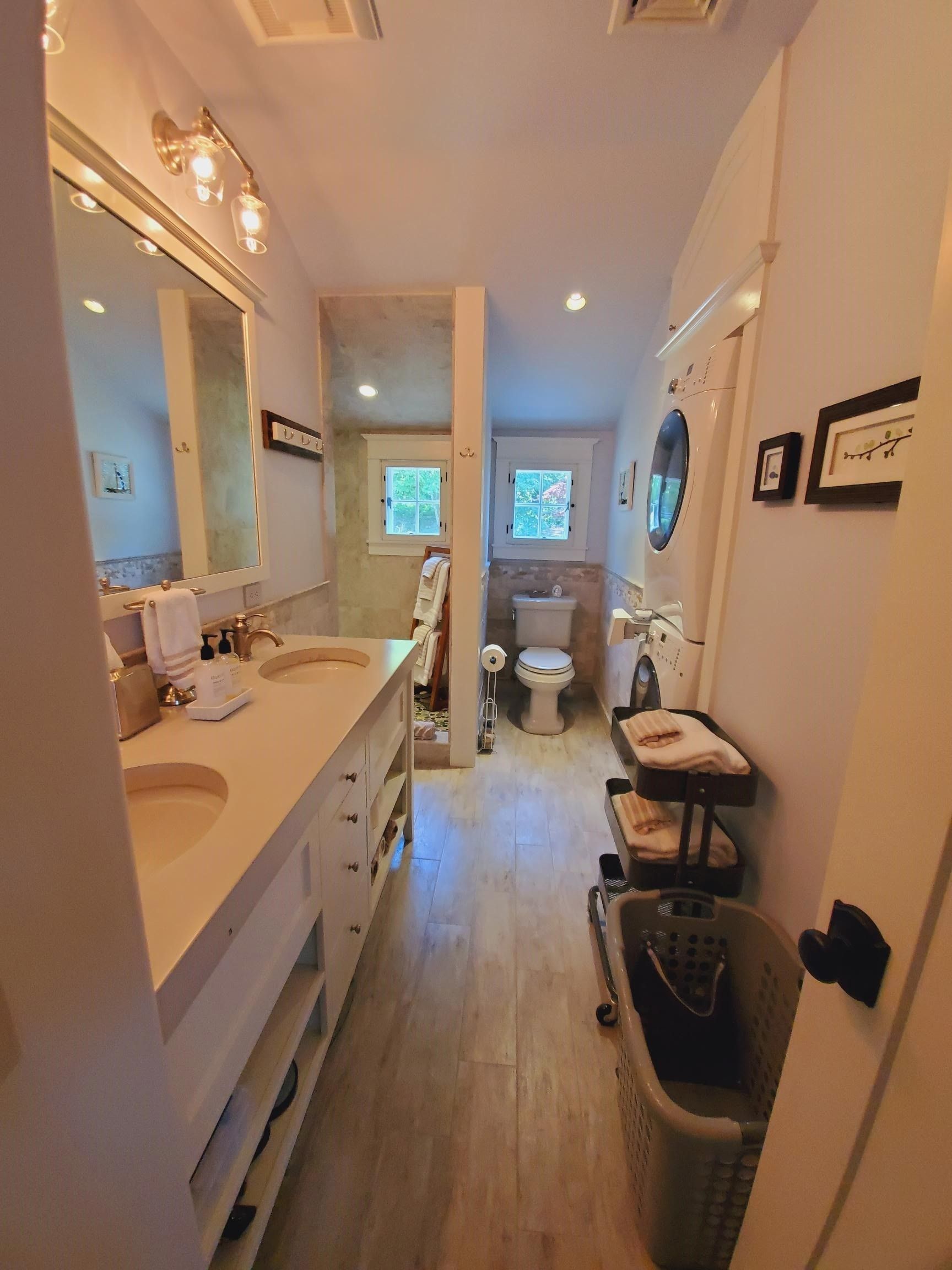 Bathroom with double vanity, toilet, and shower. Light wood floors, white walls.