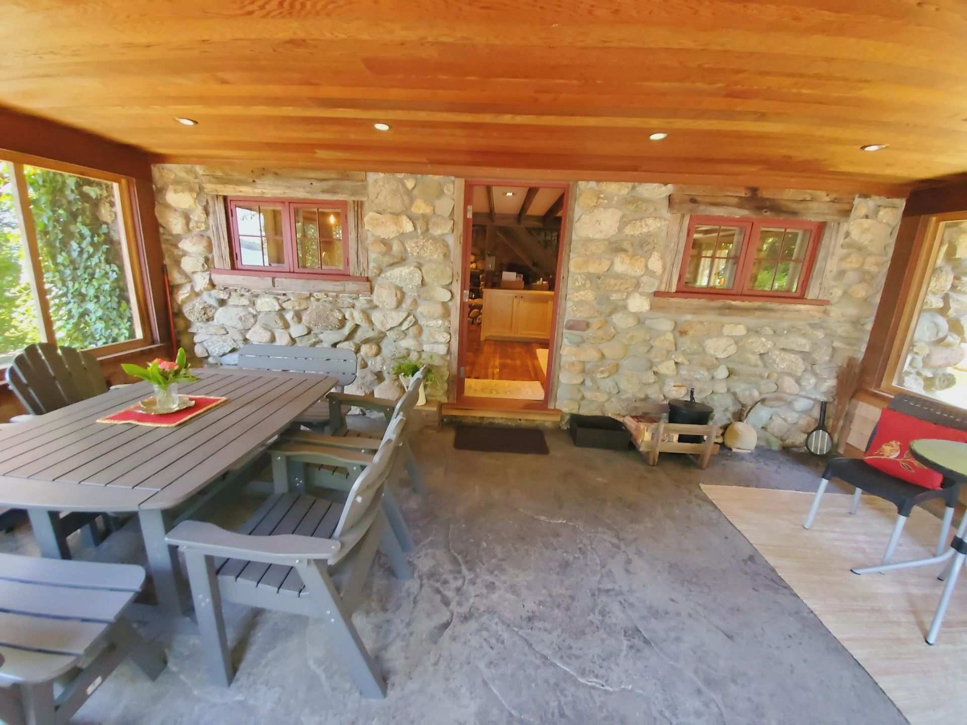Outdoor patio with stone walls, wooden ceiling, and dining table.