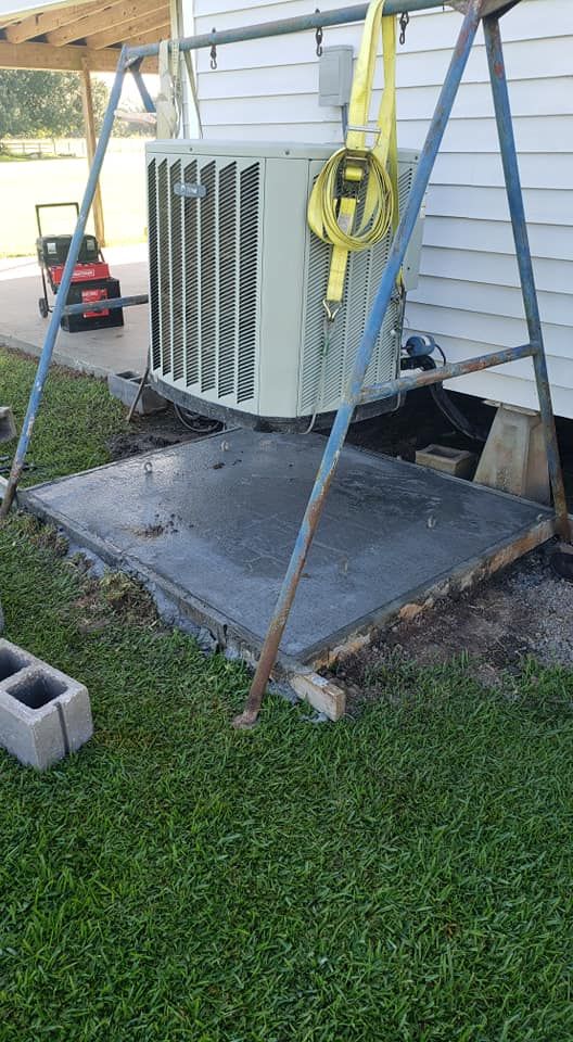 An air conditioner is sitting on top of a concrete slab next to a house.