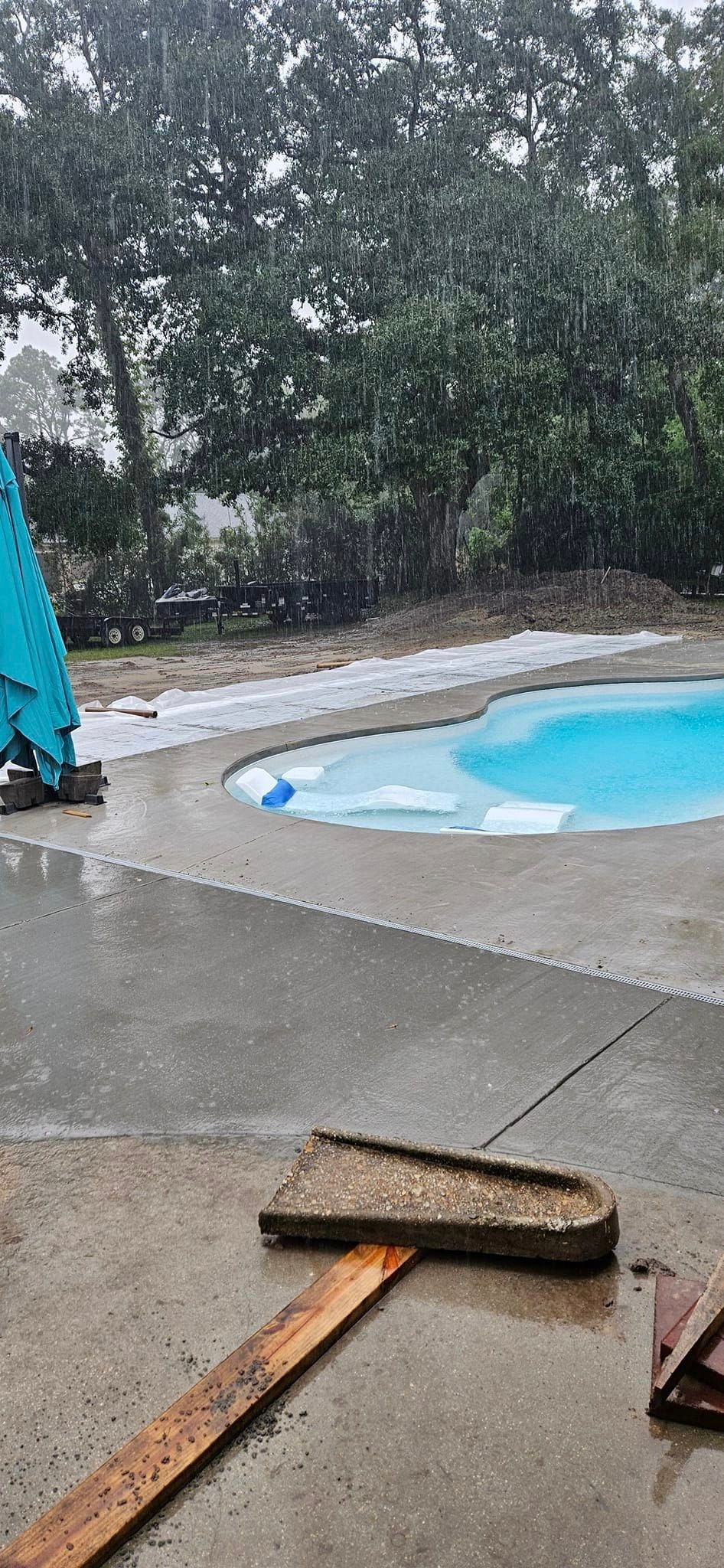 A pool with a blue umbrella and a broom on the side of it in the rain.