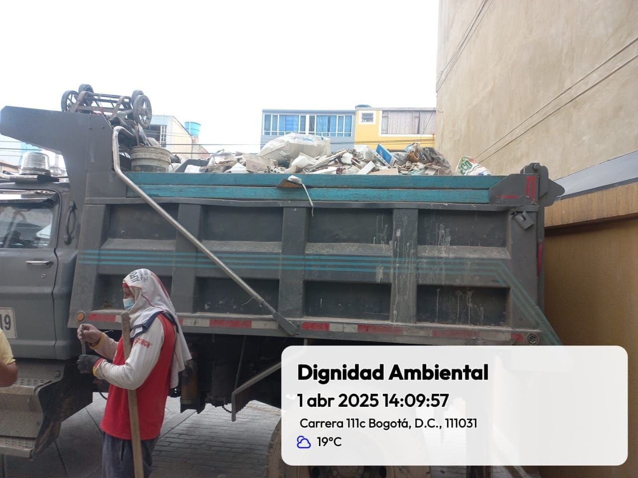 Una mujer está parada al lado de un camión de basura lleno de basura.