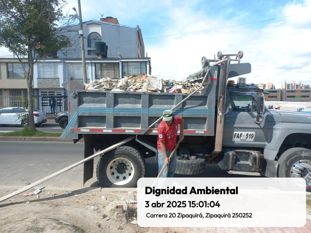 Un hombre está parado al lado de un camión volquete lleno de basura.