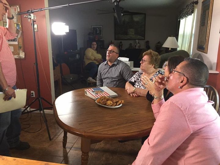 People seated around a wooden table in a living room, listening to an off-camera speaker.