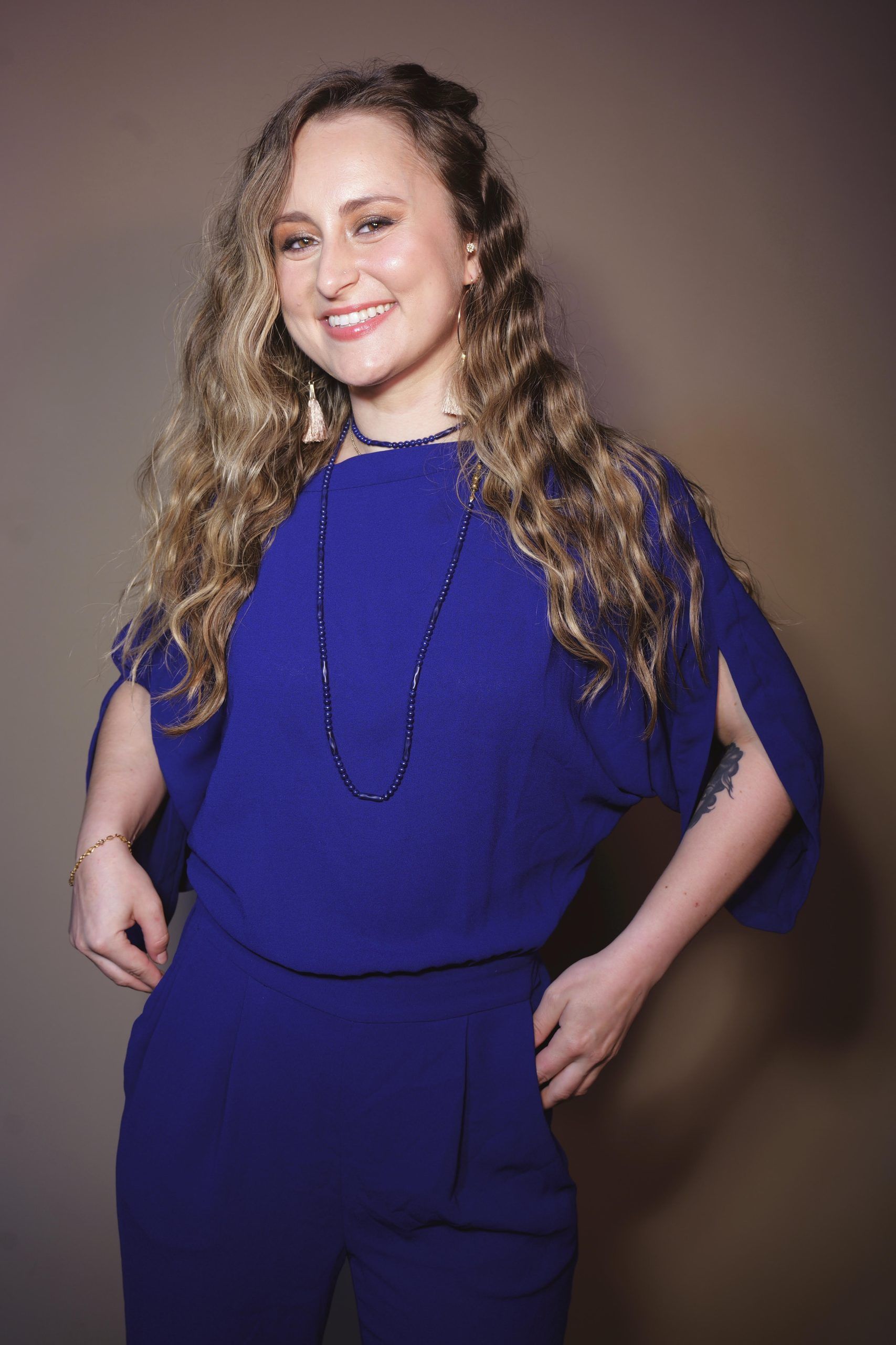 Person in a royal blue outfit smiling against a plain brown backdrop