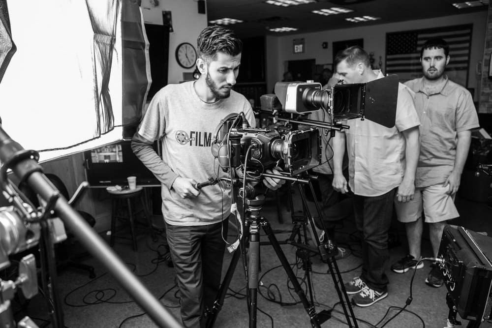 Film crew setting up a camera in a studio, with two people standing nearby.