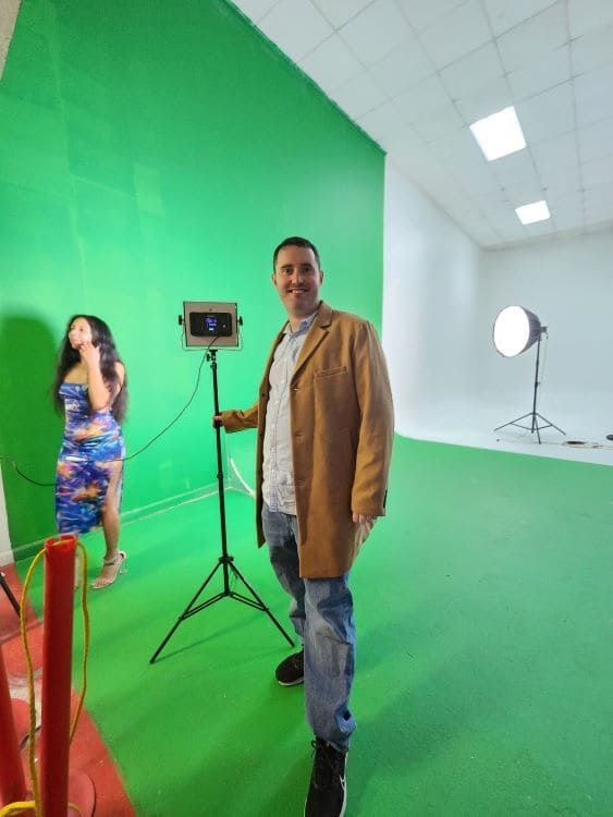 Green-screen studio with two people, a camera on a tripod, and studio lights.