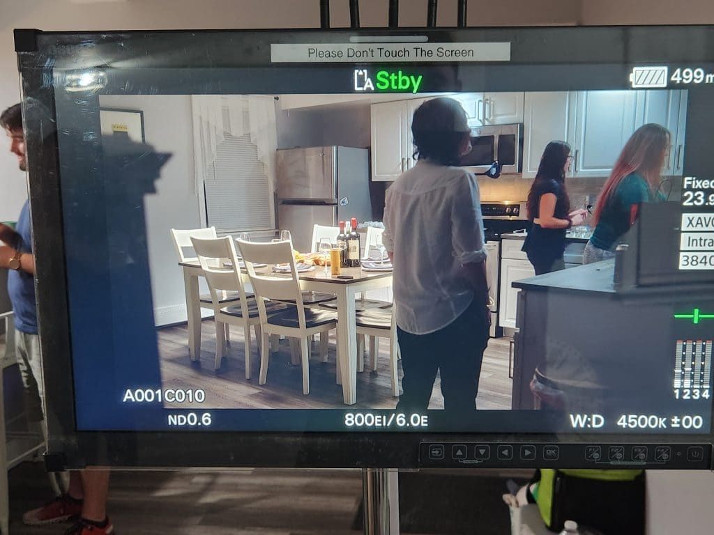 People in a kitchen, one standing at the counter while others sit around a dining table.