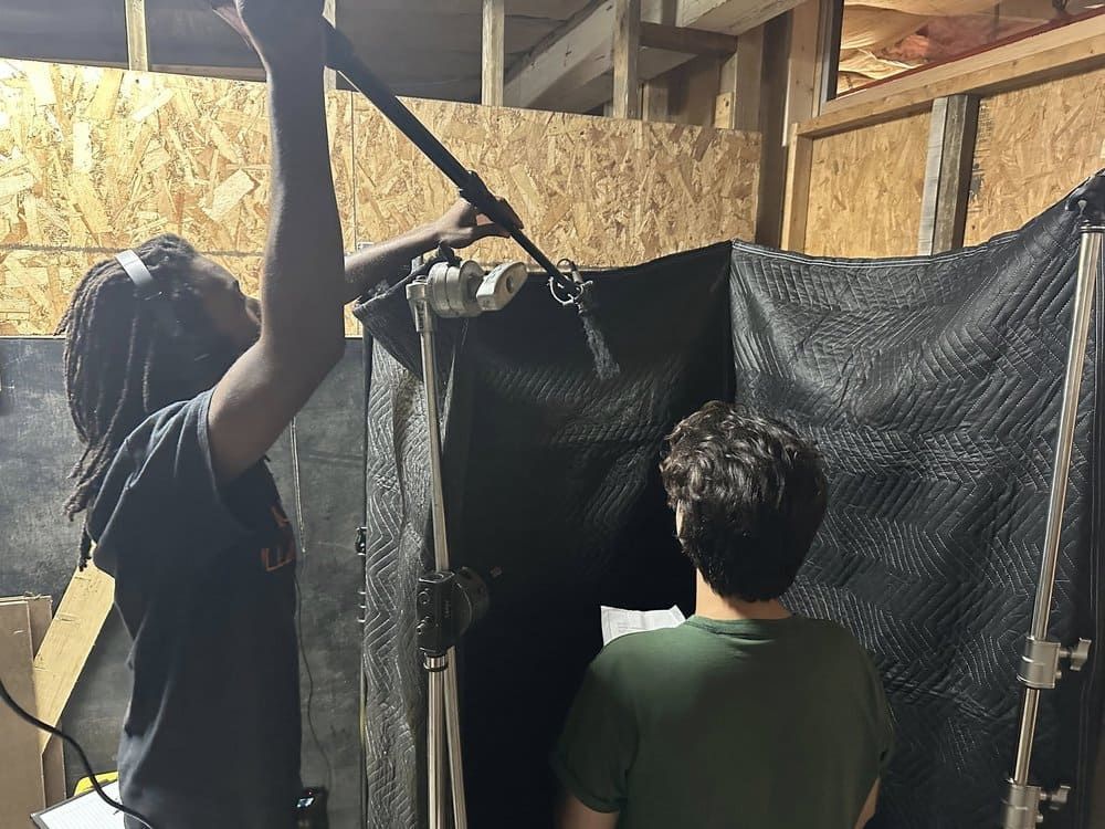 Two people stand in a wooden shed, adjusting a black hanging tarp or curtain.