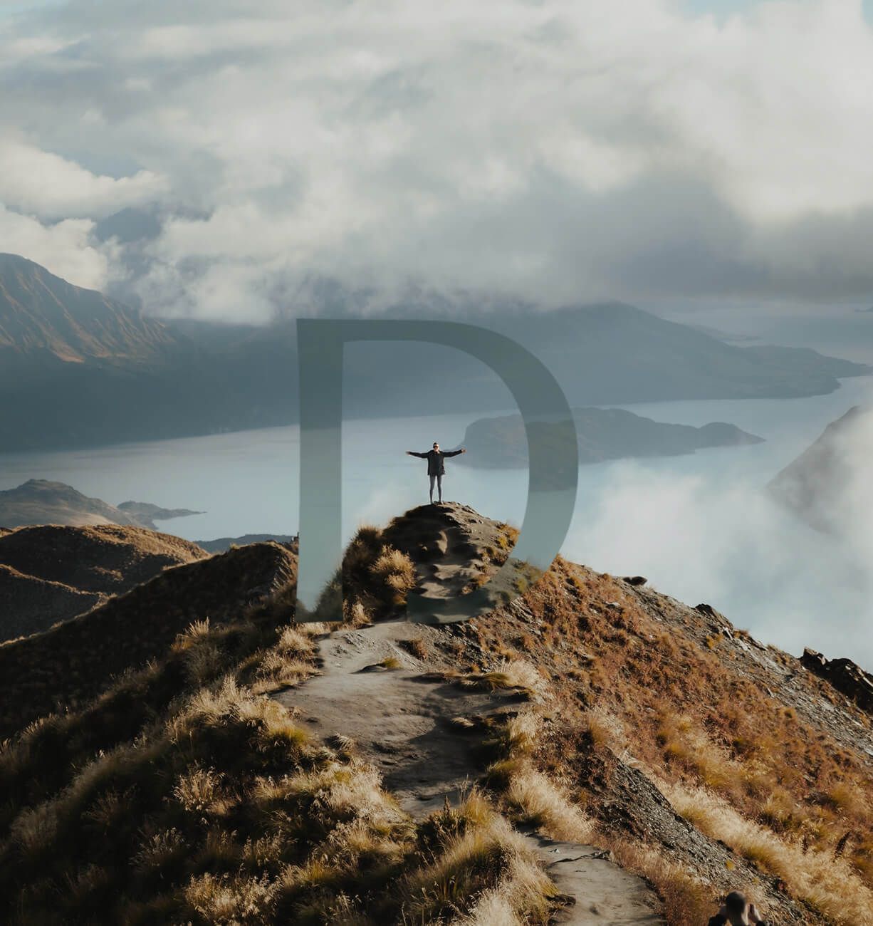 Person standing on a mountain ridge overlooking a misty valley and distant peaks
