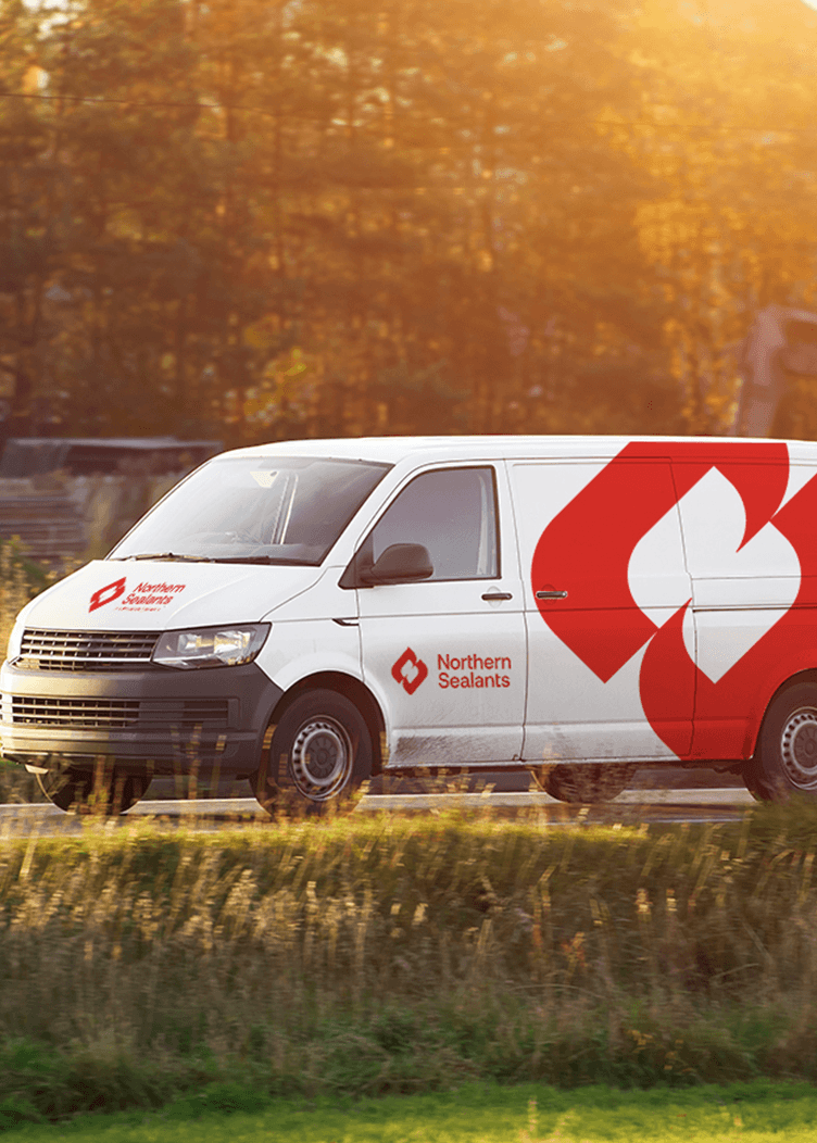 White delivery van with red logo driving on a road through a wooded area at sunset
