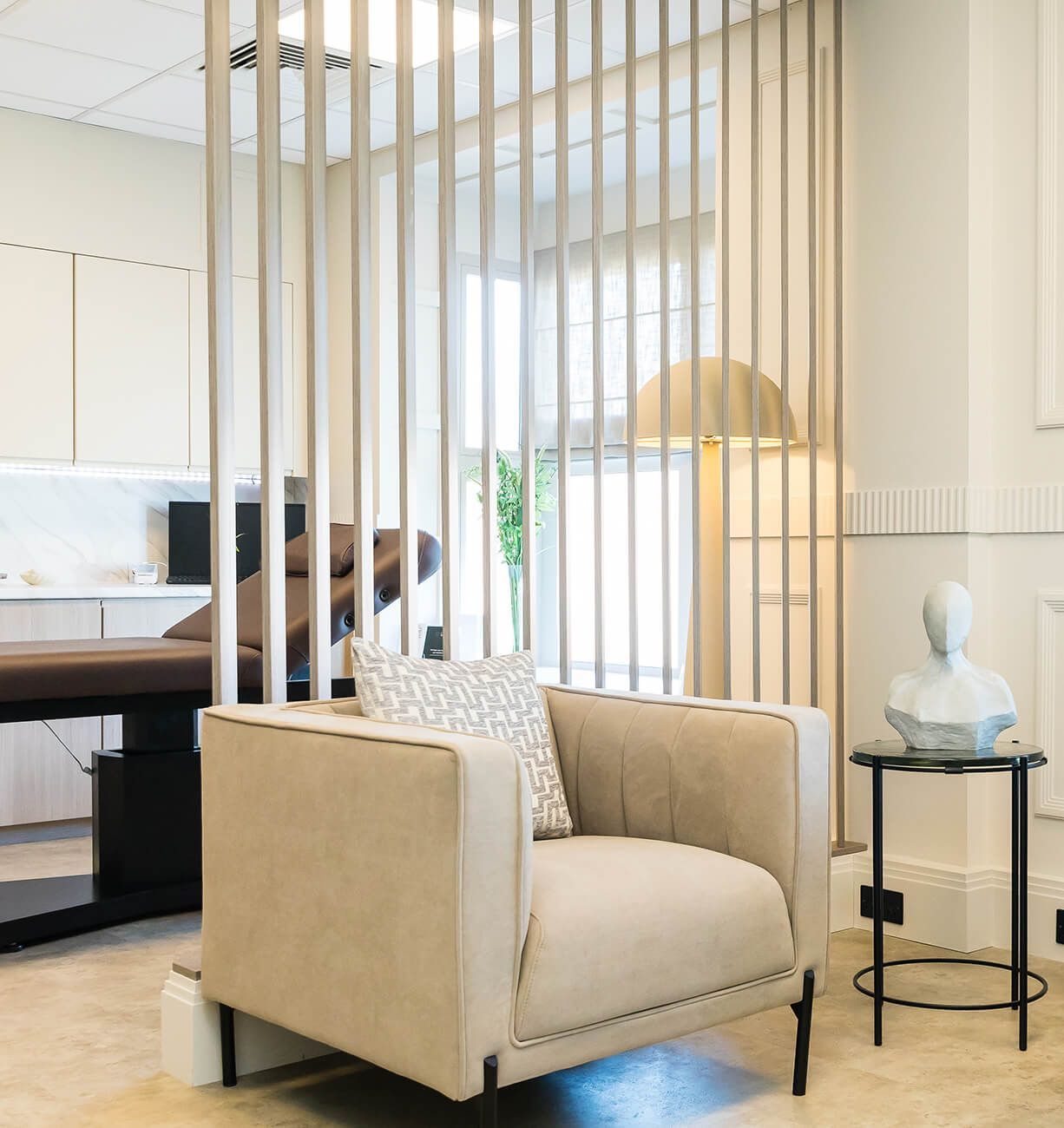 Modern living room with beige armchair, side table, lamp, and vertical wood slat divider.