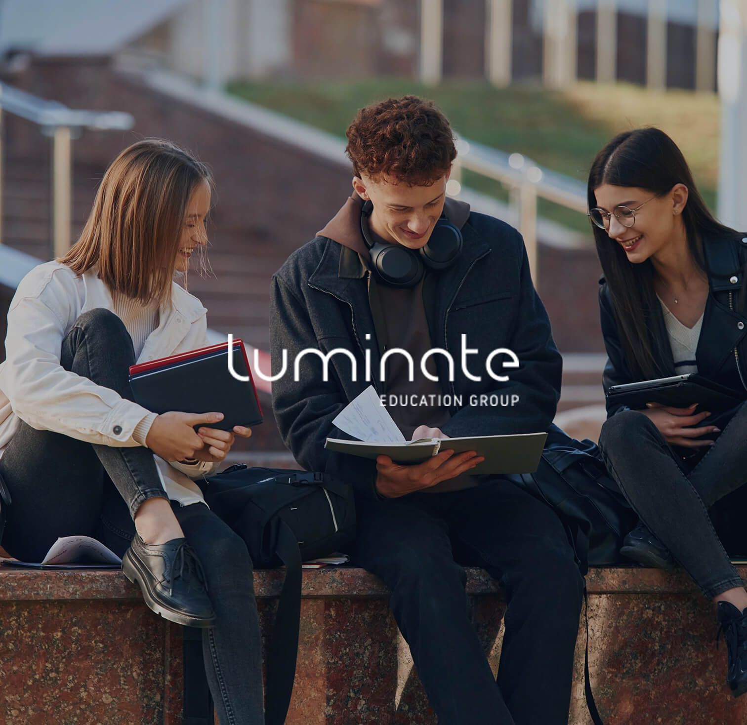 Three students sitting outdoors with laptops, centered around the Umnita Education Group logo