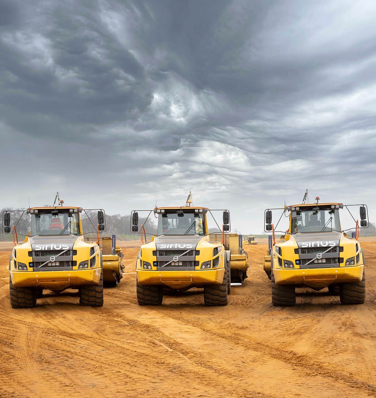 Three yellow bulldozers lined up on a dirt site under a cloudy sky