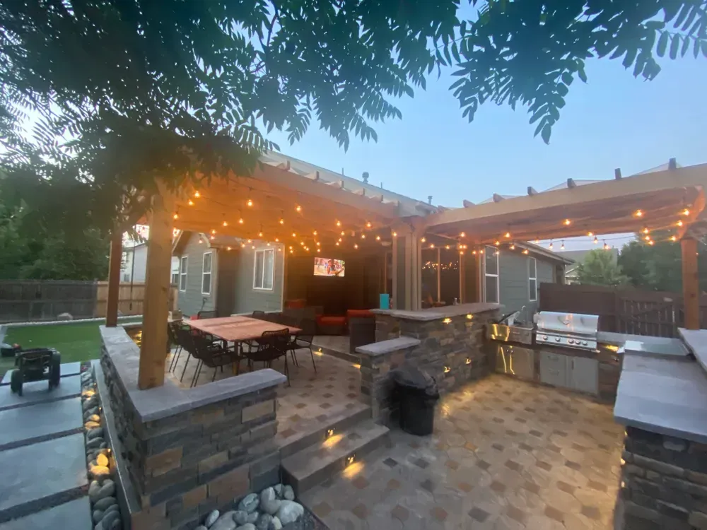 Outdoor patio with pergola, string lights, kitchen, grill, and seating area.