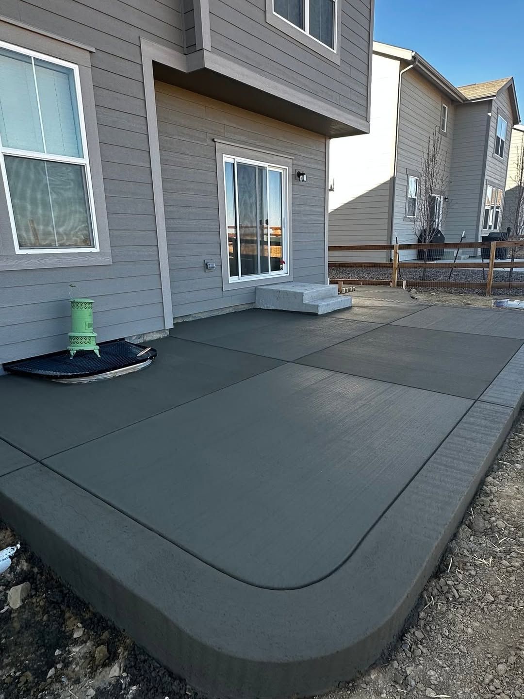 A new, gray concrete patio with rounded corners attached to the back of a two-story gray house.