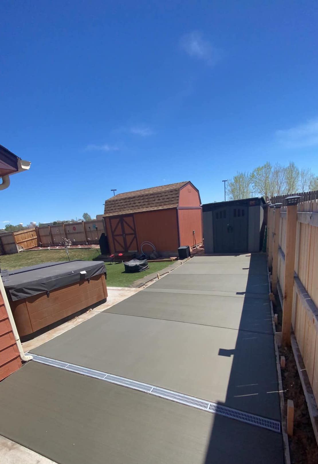 Backyard patio with concrete paving, storage sheds, and a wooden fence under a clear blue sky