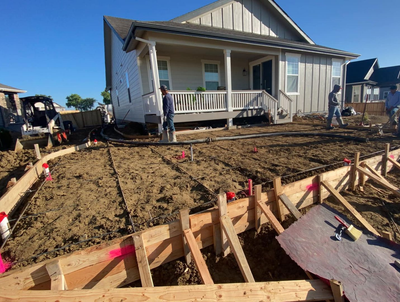backyard patio concrete slab under construction with workers, dirt yard, and wooden formwork in the foreground