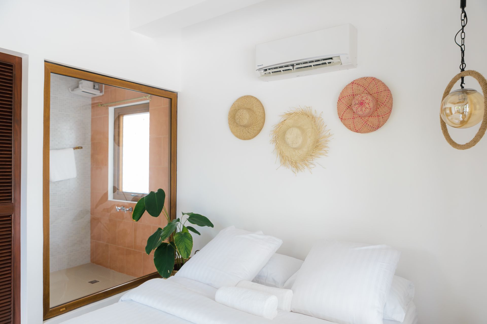 A bedroom with a bed , mirror and straw hats on the wall.