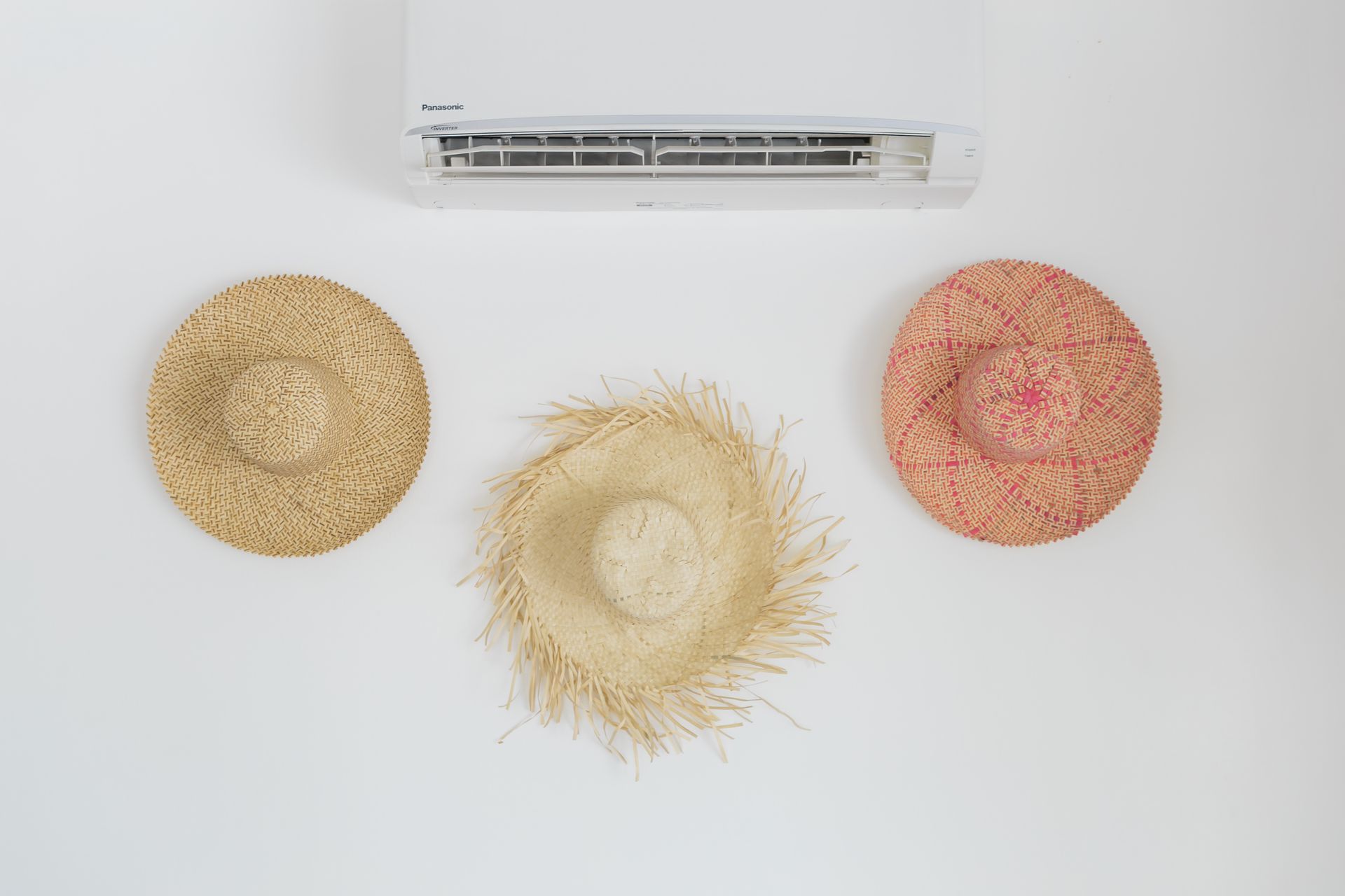 Three hats are hanging on a wall next to an air conditioner.