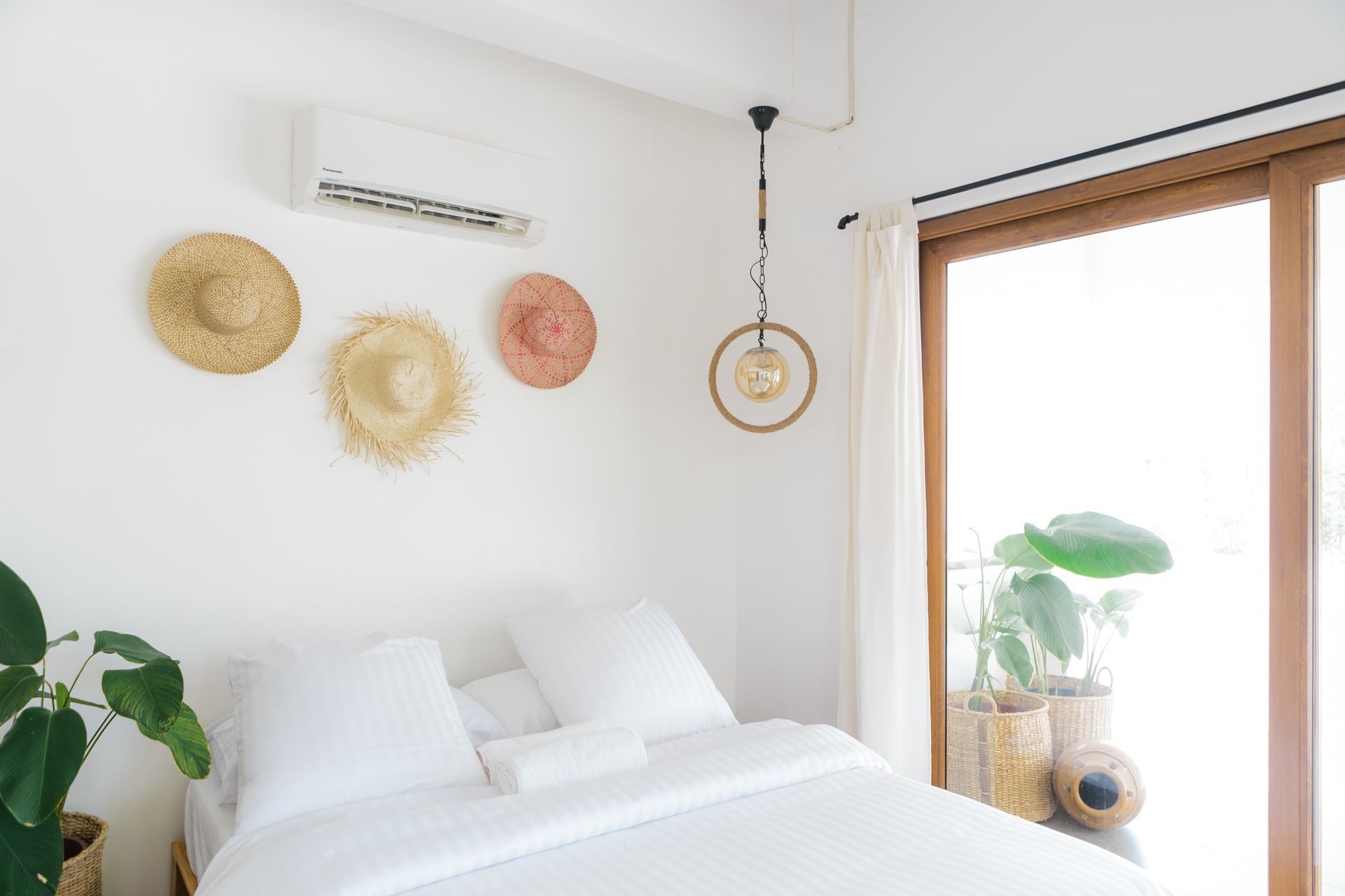 A bedroom with a bed , straw hats hanging on the wall and a window.