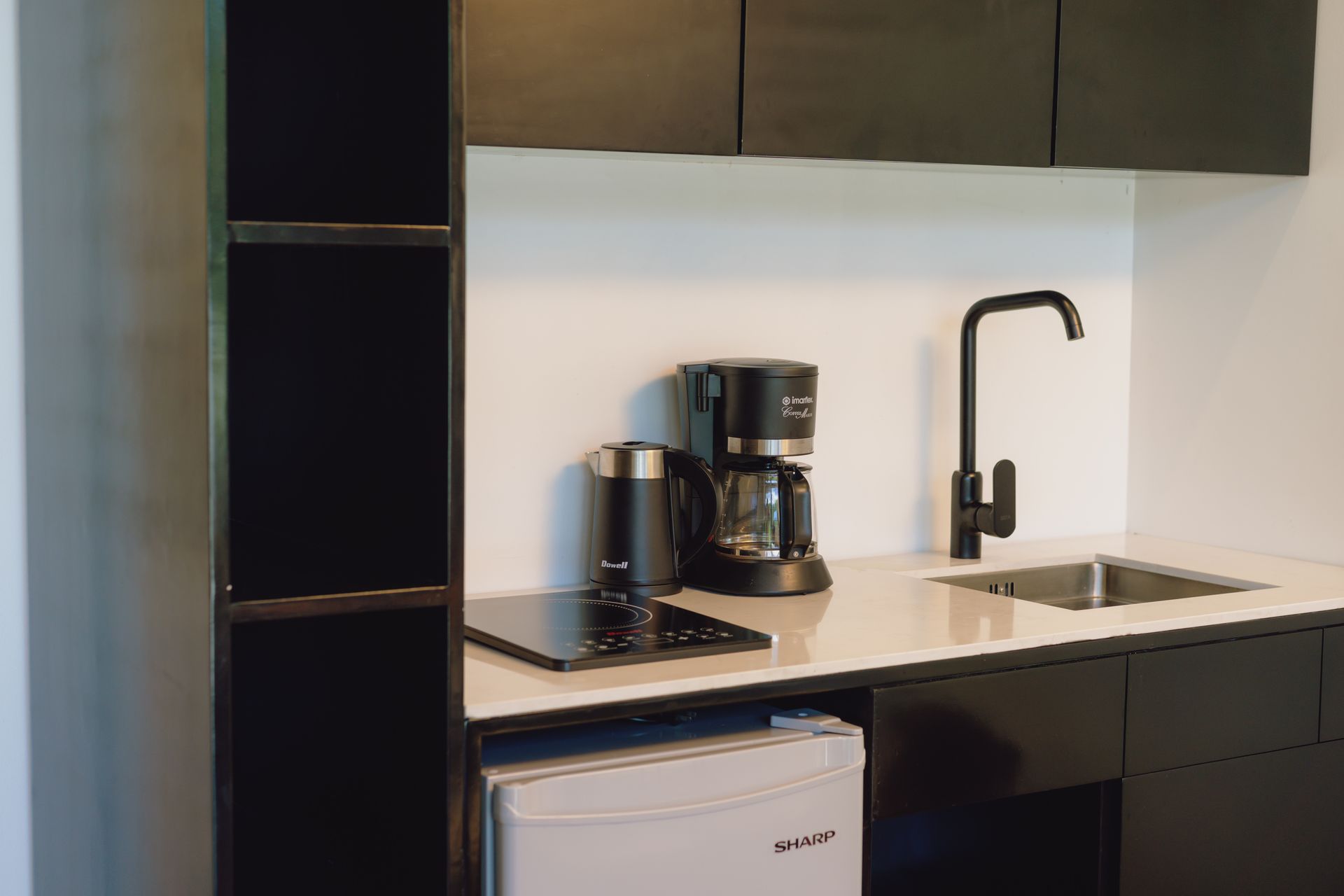 A kitchen with black cabinets , a sink , a coffee maker , and a refrigerator.