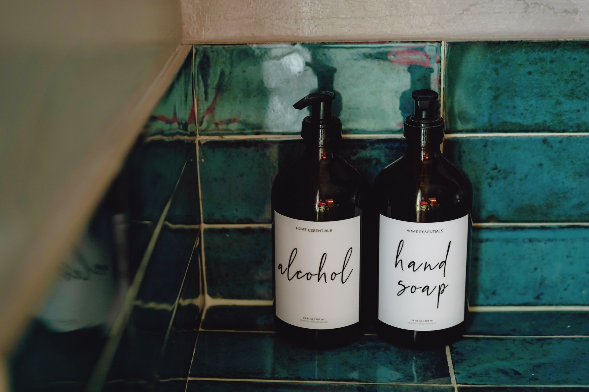 Two bottles of alcohol and hand soap on a tiled counter
