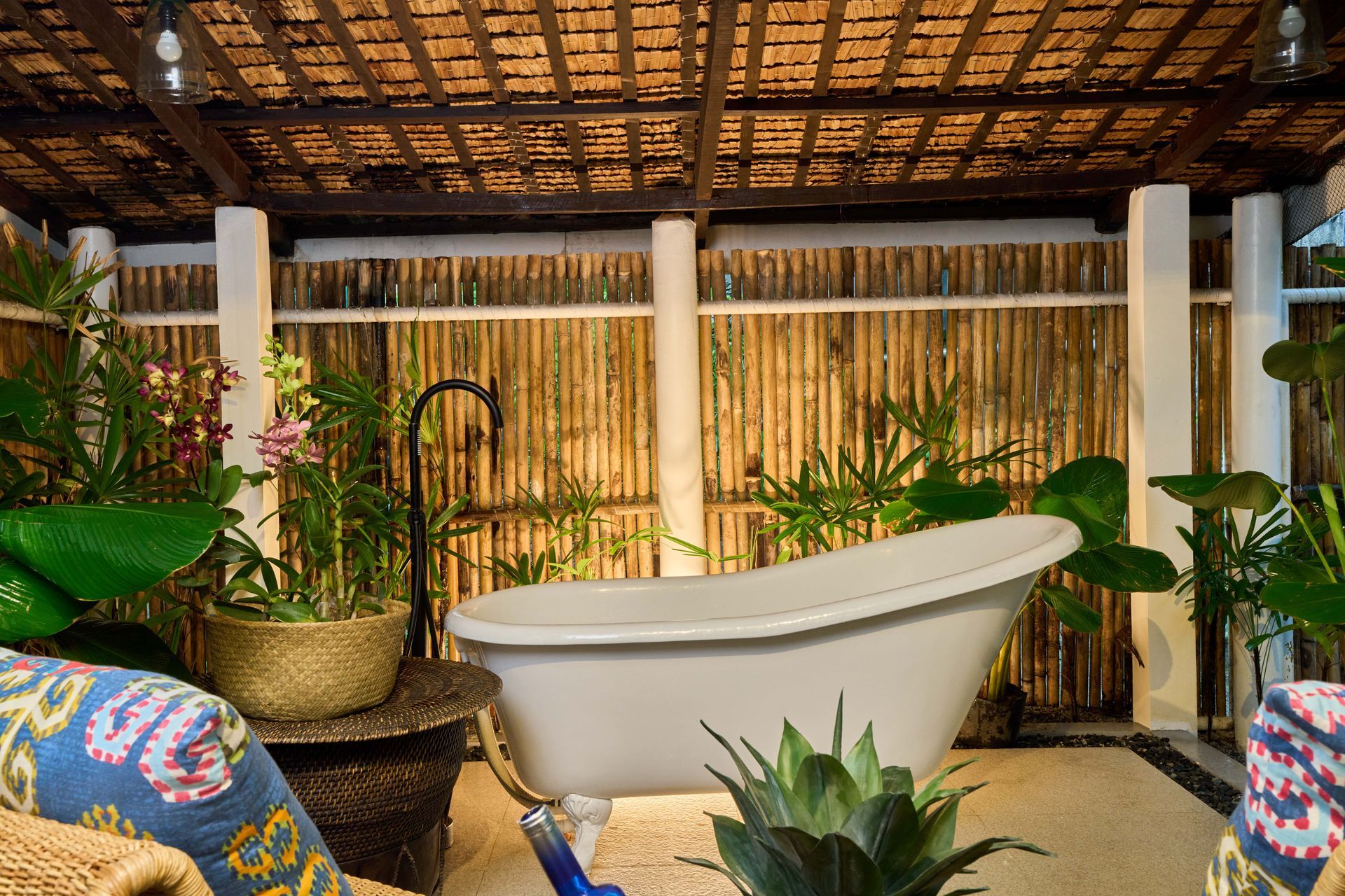 A white bathtub is surrounded by plants and a bamboo fence.