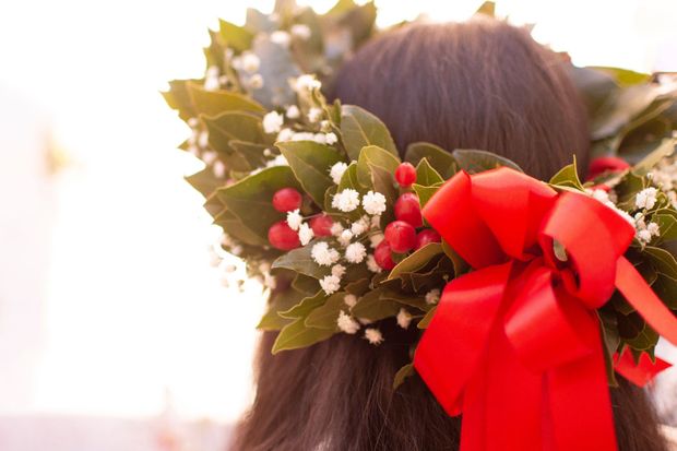 Donna dai capelli scuri, che indossa una corona d'alloro con bacche rosse e un grande fiocco rosso.