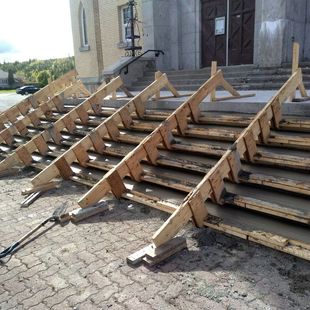 Une structure en bois soutient des marches en béton menant à l'entrée du bâtiment. Les travaux sont en cours.