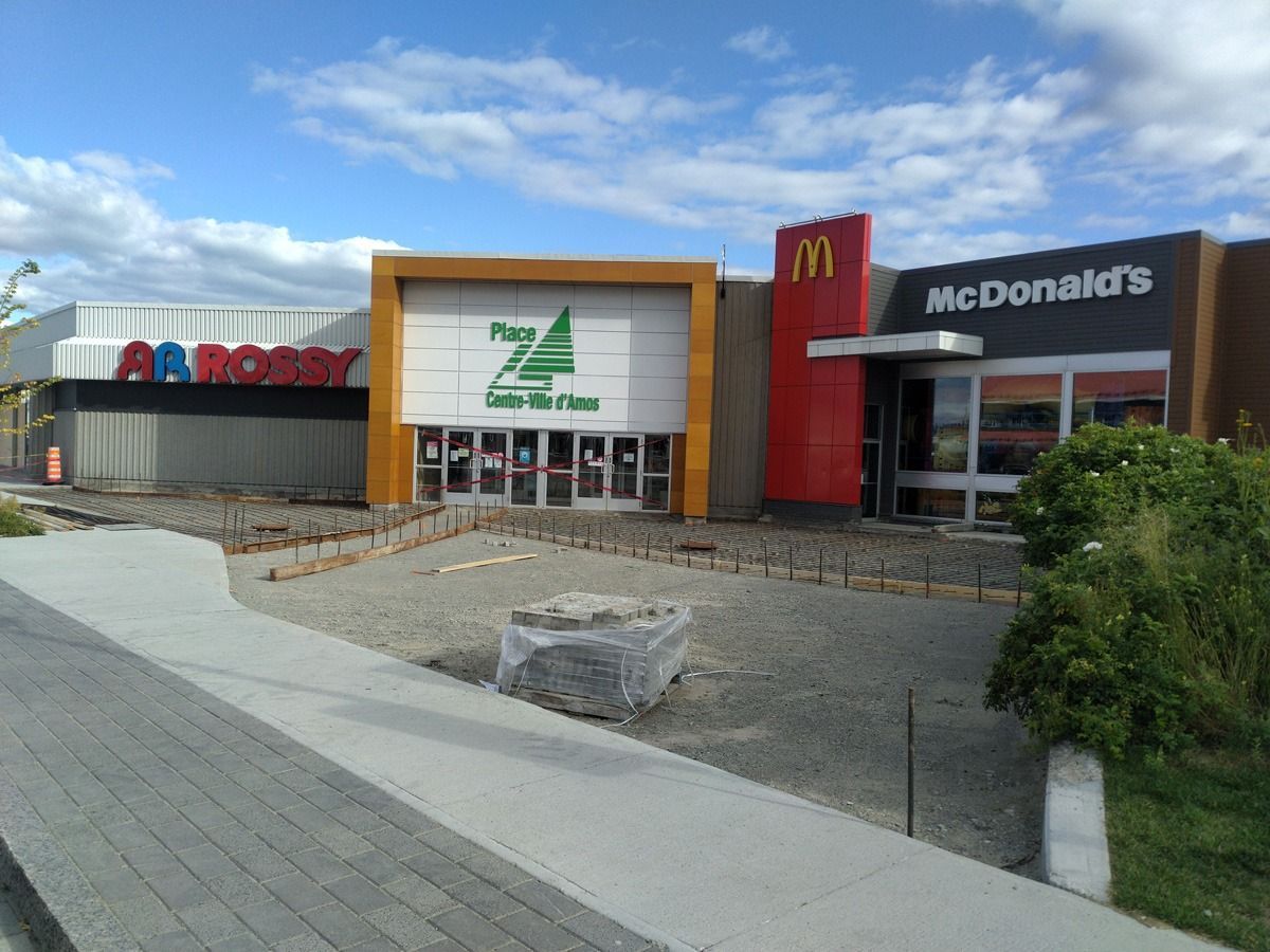 Vue extérieure d'un restaurant McDonald's situé à côté de la Plaza Los Puentes et d'un magasin à l'enseigne sombre. Le trottoir semble être en travaux.