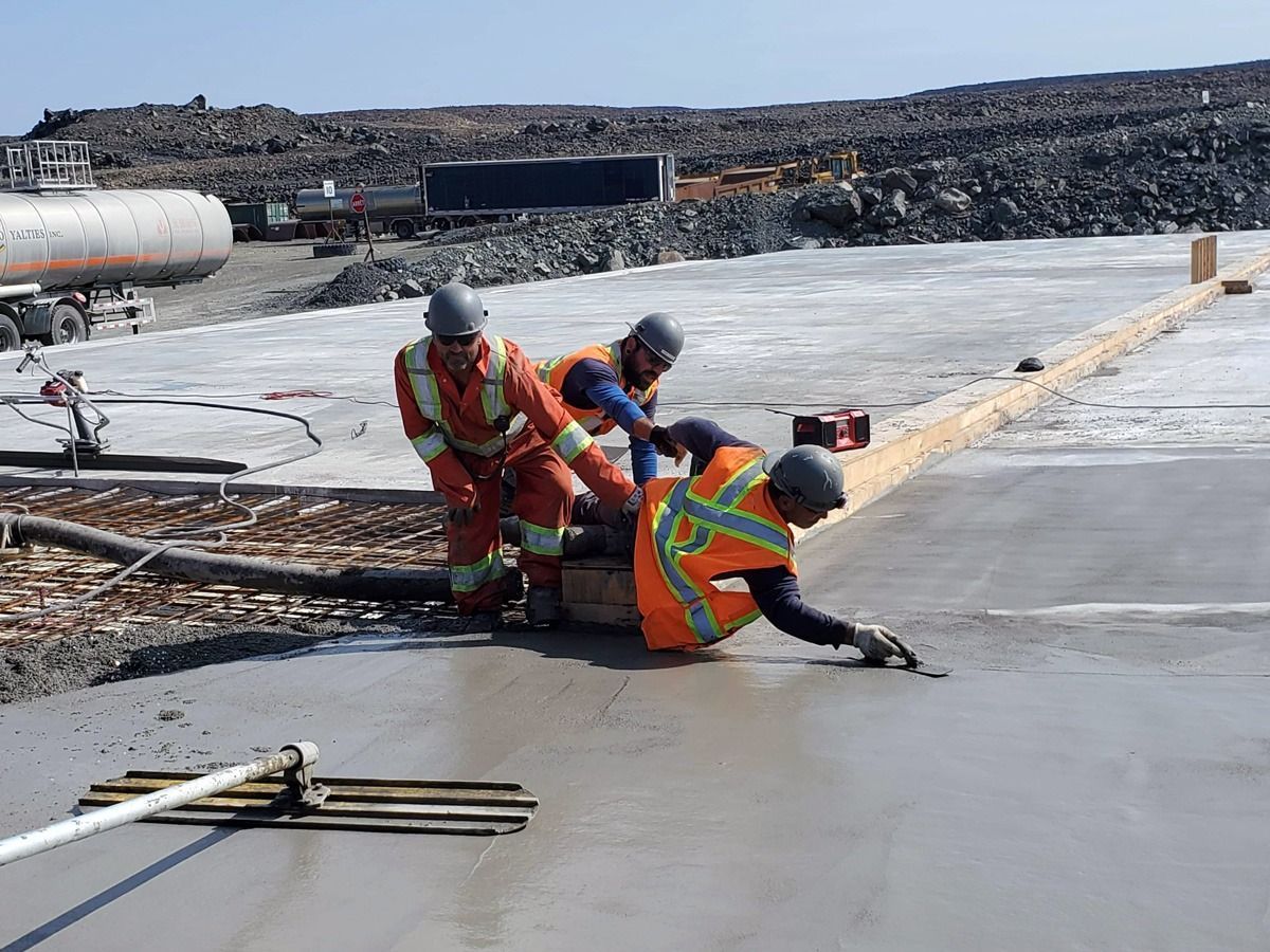 Trois ouvriers du bâtiment lissent du béton frais avec des outils sur un chantier.