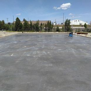 Dalle de béton fraîchement coulée en extérieur, avec une machine bleue visible.
