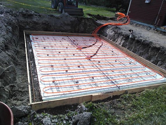 Fosse de construction encadrée avec tubes de chauffage radiant rouges posés sur une isolation blanche, prête pour le coulage du béton.