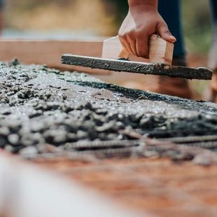 Une personne utilise une truelle pour lisser du béton frais, posé sur des barres d'armature, dans un contexte de construction extérieure.